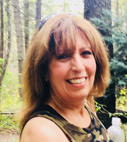 A woman with long hair and a smile in the woods.