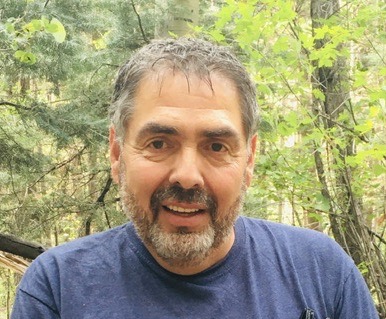 A man with grey hair and beard wearing blue shirt.