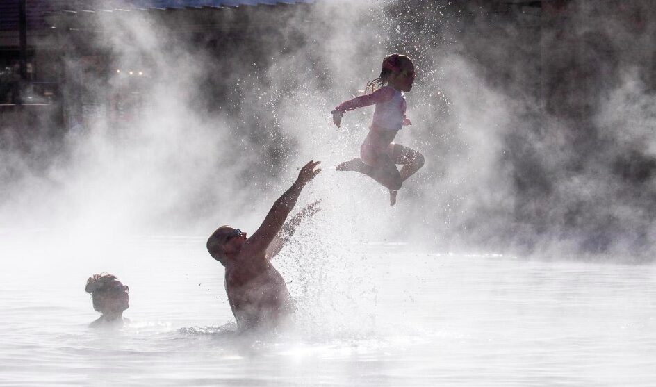 dad tossing young child into the hot springs water with the mother behind looking on