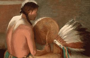 Native Indian man playing the drums and a headdress of feathers sits beside him