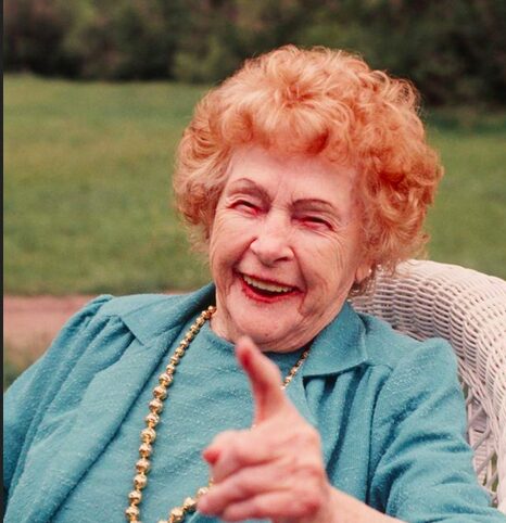 An older woman sitting in a chair with her finger up.