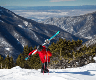 man climbing taos mountain with skis on his back