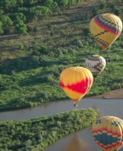 4 hot air balloons flying over the Rio Grande River near ABQ